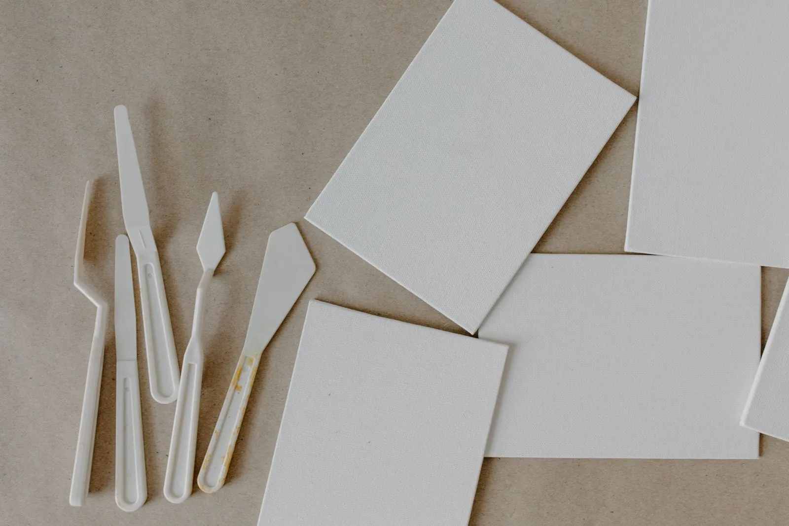 Top view of art supplies including palette knives and blank canvases on a brown background.